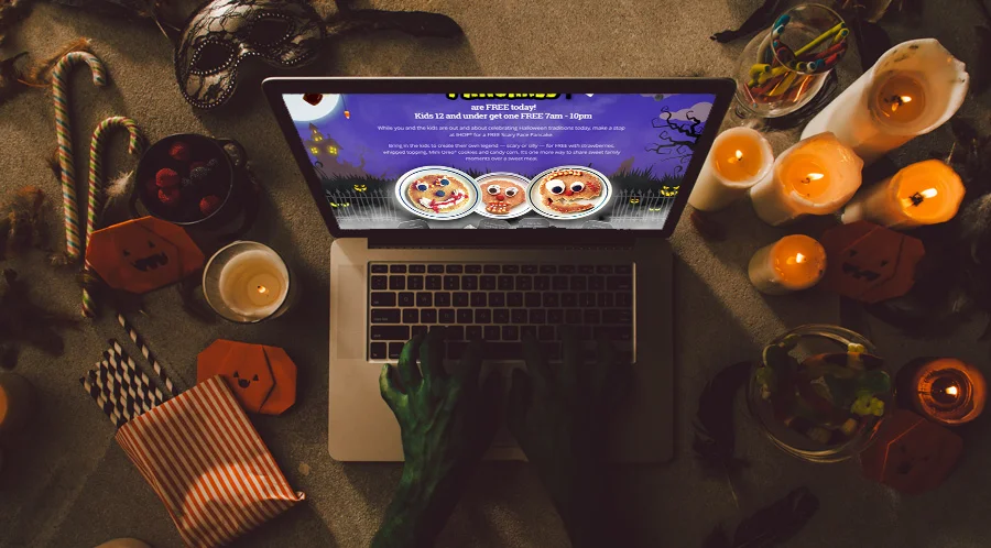 Laptop showing the Scary Face Pancakes page on a Halloween table with candles, candy and a monster hand